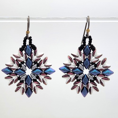 An image of two earrings hanging on a display. The combination of beads appears like a star quilt pattern.